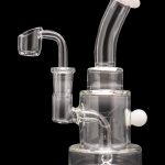 Clear glass dab rig with a quartz banger and white accents, isolated on a black background.