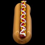 Glass pipe shaped like a hot dog with mustard and relish, against a black background.