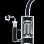 Clear glass water pipe (rig) with intricate percolator and accompanying dab nail, isolated on black.