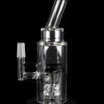 Clear glass water pipe (rig) with intricate bubbler design, reflecting on a glossy black surface.