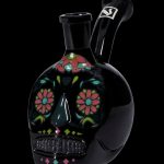 Black glass skull-shaped water pipe with colorful floral Day of the Dead-inspired designs.