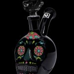 Black glass skull-shaped water pipe with colorful floral designs, isolated on a black background.