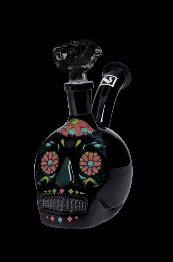 Black glass skull-shaped water pipe with colorful floral designs, isolated on a black background.