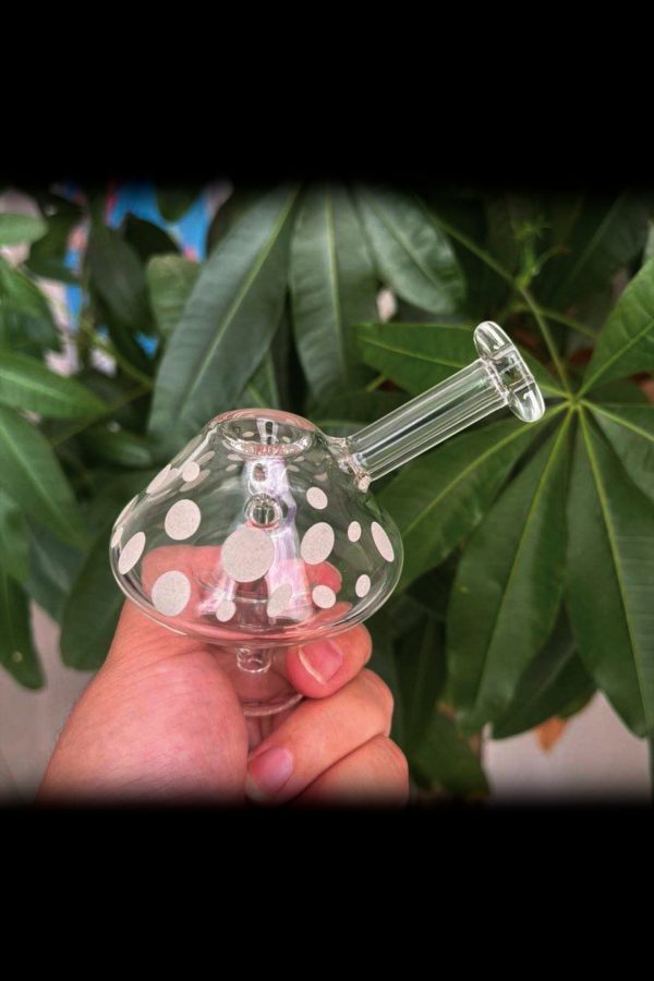 A hand holding a patterned glass bubbler with a green plant background.