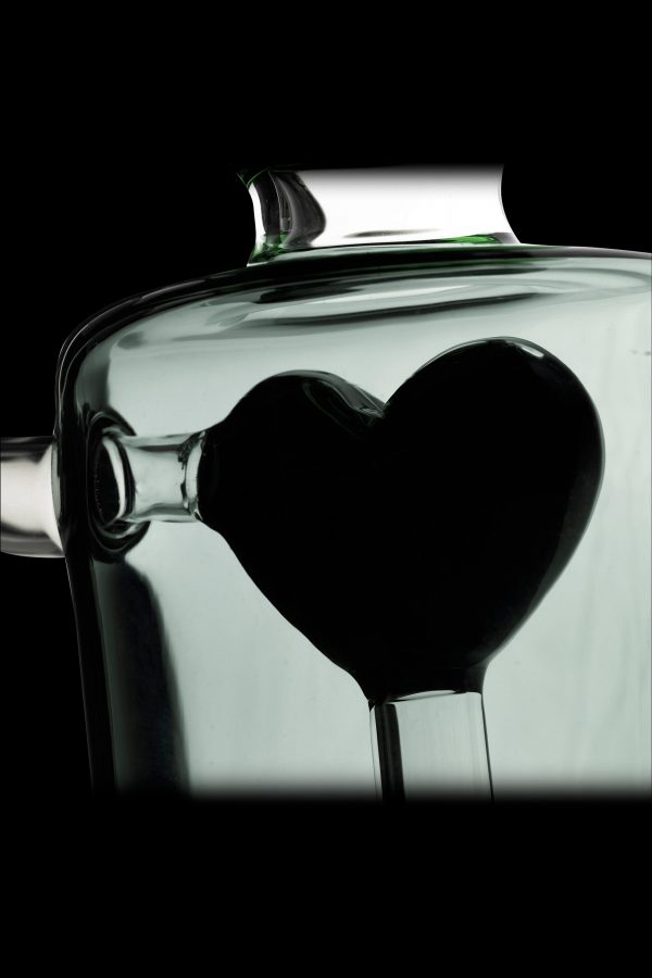 A glass cannabis water pipe shaped like a heart, silhouetted against a pale green background.