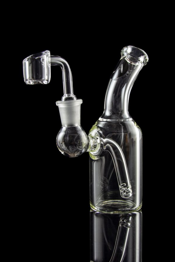 Clear glass dab rig with quartz banger, reflecting on a dark surface.