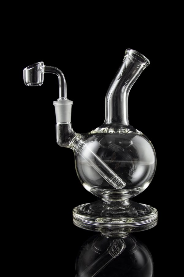 Clear glass dab rig with a quartz nail, reflecting on a black surface.