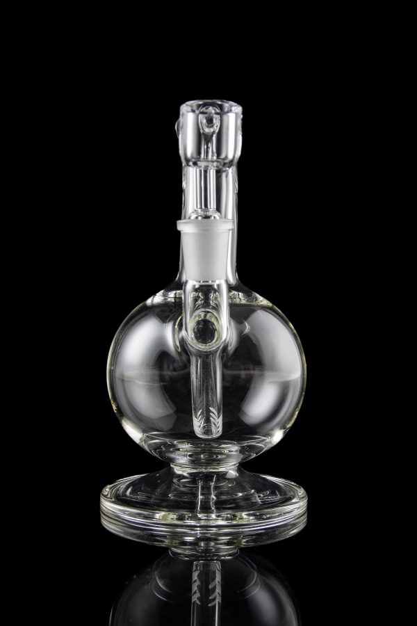 Clear glass water pipe (rig) with spherical body and intricate internal pathways, reflecting on a dark surface.