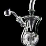 Clear glass water pipe (rig) with intricate bubbler design and a separate quartz nail for concentrates, displayed on a reflective surface against a black background.