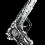 Clear glass pipe shaped like a handgun, reflecting on a black surface.
