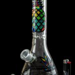 A colorful glass bong with a patterned design, accompanied by glass smoking accessories on a dark background.
