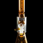 Amber glass water pipe (rig) with intricate clear glass percolator and “Pulsar” logo, isolated on black.