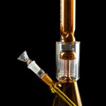 Amber glass water pipe (bong) with intricate percolator and detachable bowl, isolated on black.