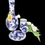 Ornate porcelain cannabis water pipe and accessories with white roses on a black background.