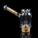 Clear glass bubbler with a wooden mouthpiece and red accent, reflecting on a glossy black surface.