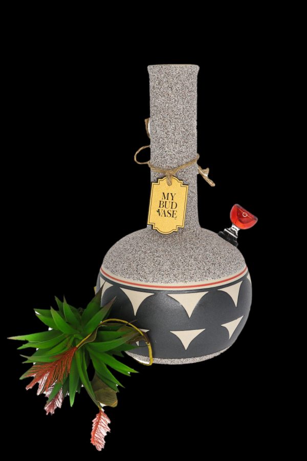 A patterned ceramic water pipe (“Bud Vase”) with a tag and flowering plant beside it, against a black background.