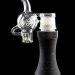 Clear glass bubbler attachment connected to a black electronic dab rig, reflecting on a glossy surface.