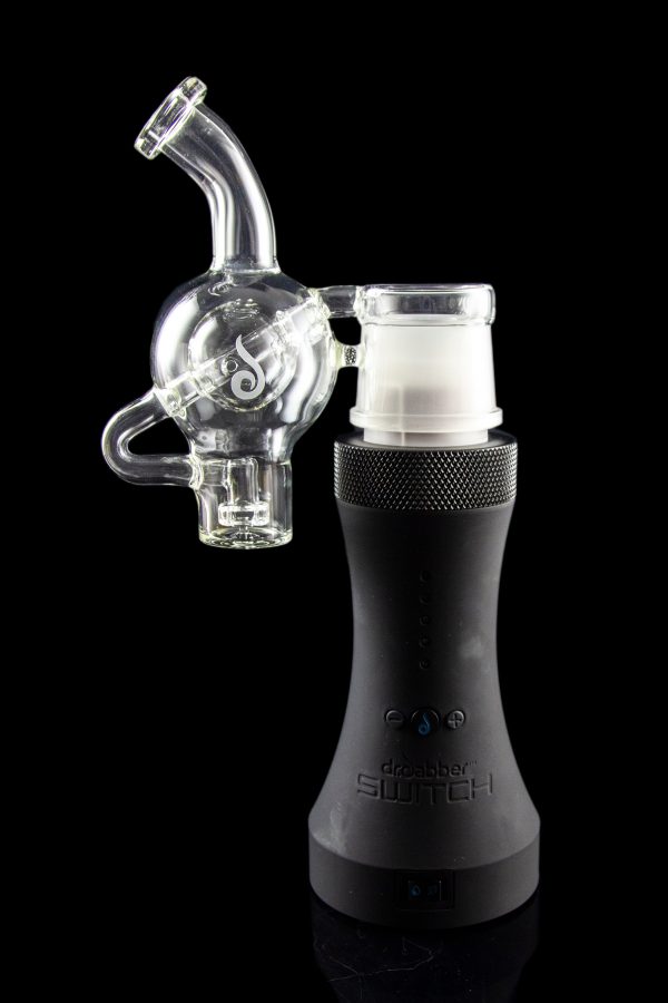 Clear glass bubbler attachment connected to a black electronic dab rig, reflecting on a glossy surface.