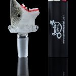 A studio shot displays the Empire Glassworks "Jawsome" Bowl Piece, with a shark-themed design reflected on a mirrored surface.