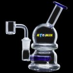Clear glass dab rig with blue accents and a quartz nail, branded "ATOMIK".