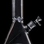 Glass bong with a flared base and purple mouthpiece, isolated on black.