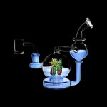 Blue glass water pipe with sculpted cannabis-themed artwork inside a spherical chamber.