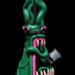 Green glass monster-themed water pipe with pink accents, displayed against a black background.