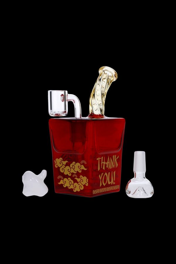Red glass bubbler shaped like a Chinese takeout container with ornate gold designs, alongside a white glass mushroom and bubbler, on a black background.