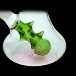 Green glass bubbler with a sculpted dragon design, set against a pink backdrop.