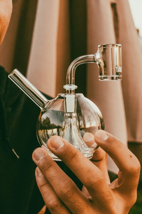 A person holds a clear glass bubbler/water pipe, often used for cannabis consumption."